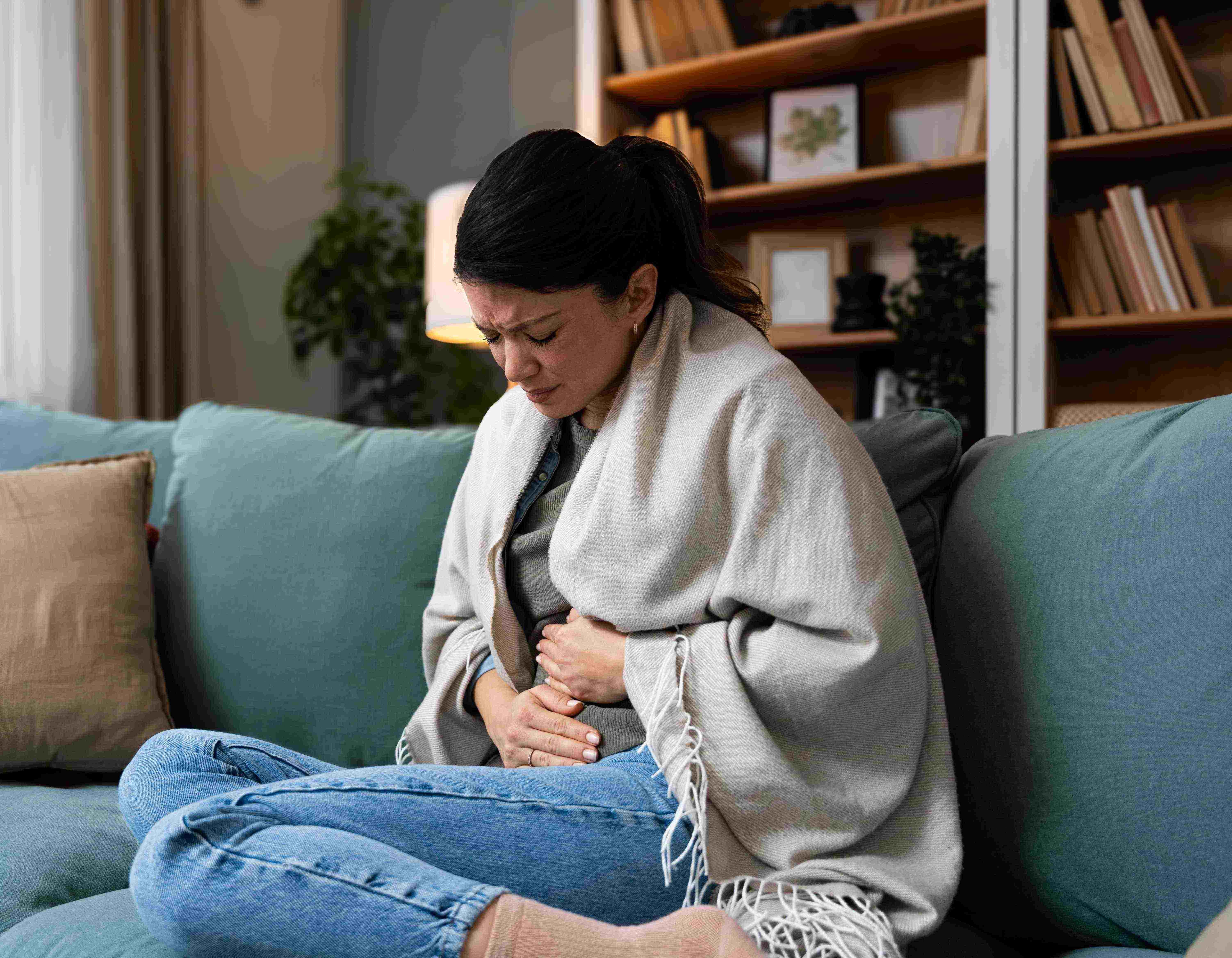 Frau mit Bauschmerzen sitzt auch dem Sofa und hält sich den Bauch