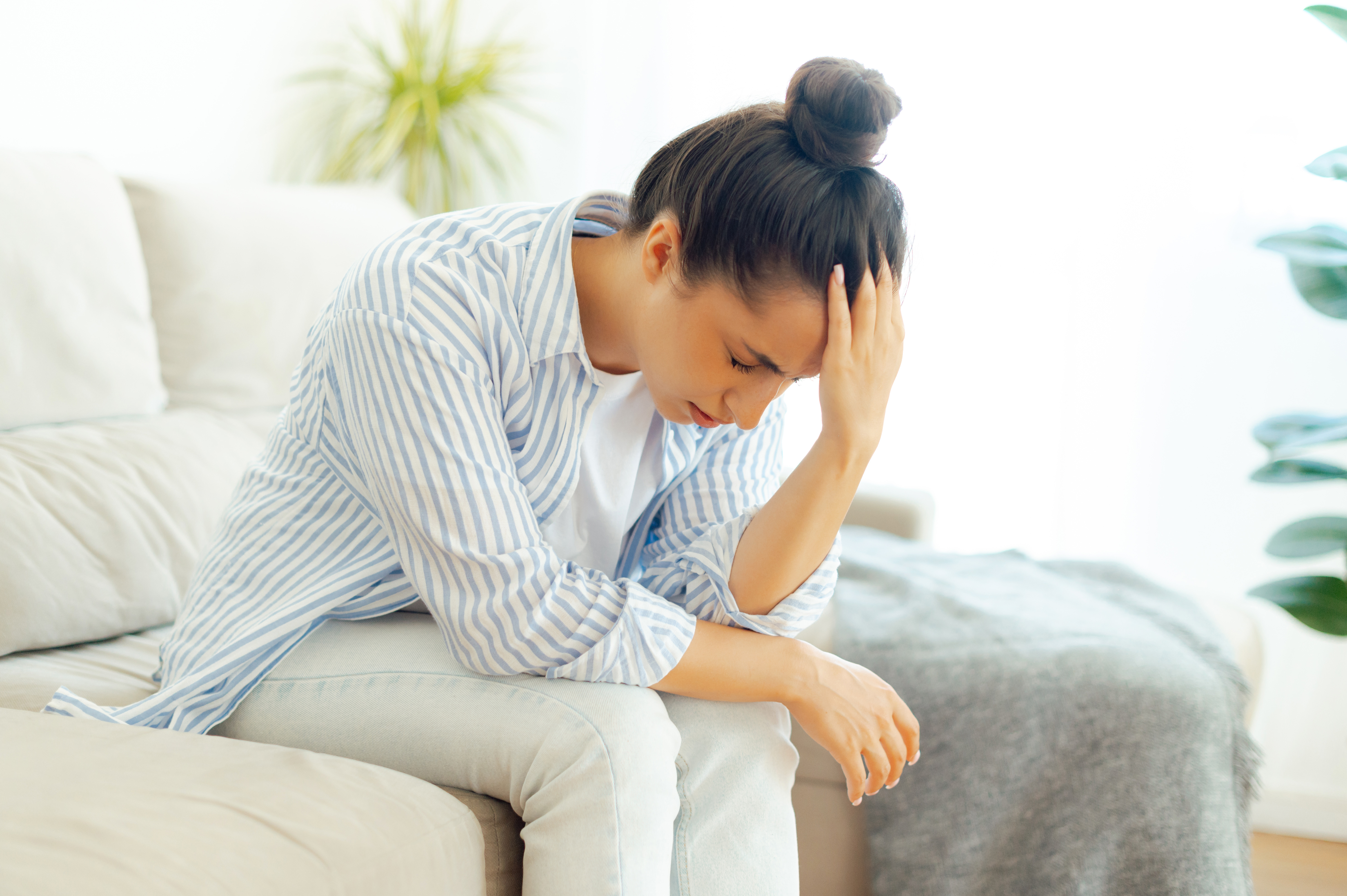 Frau sitzt auf dem Sofa und hält sich den Bauch wegen ihrer Verdauungsprobleme