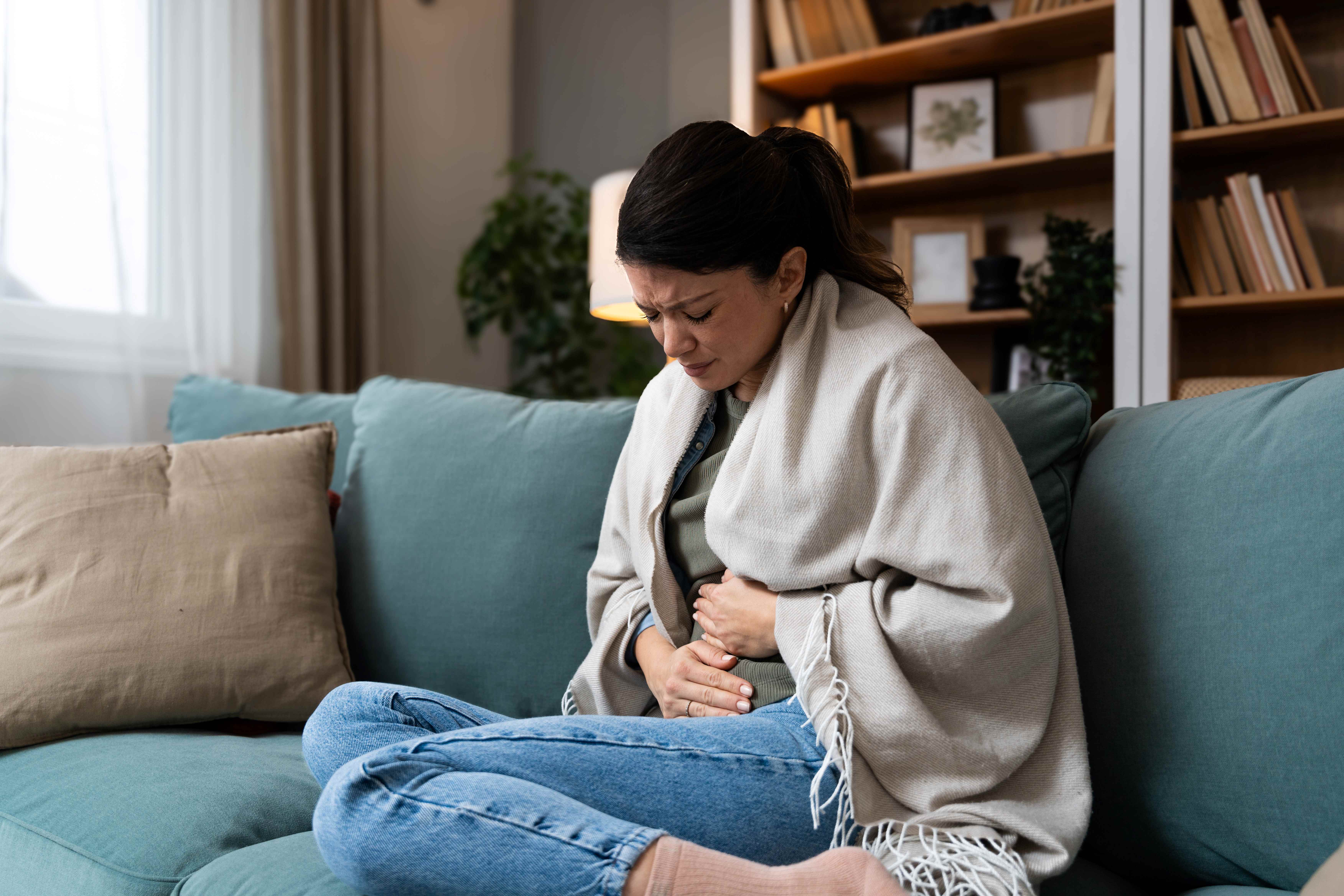 Frau sitzt auf dem Sofa und hält sich den Bauch wegen ihrer Verdauungsprobleme